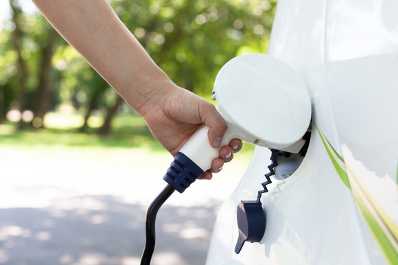 A person charging a white electric vehicle. 