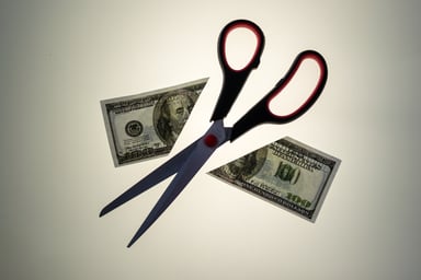 Scissors cutting hundred dollar bill in half