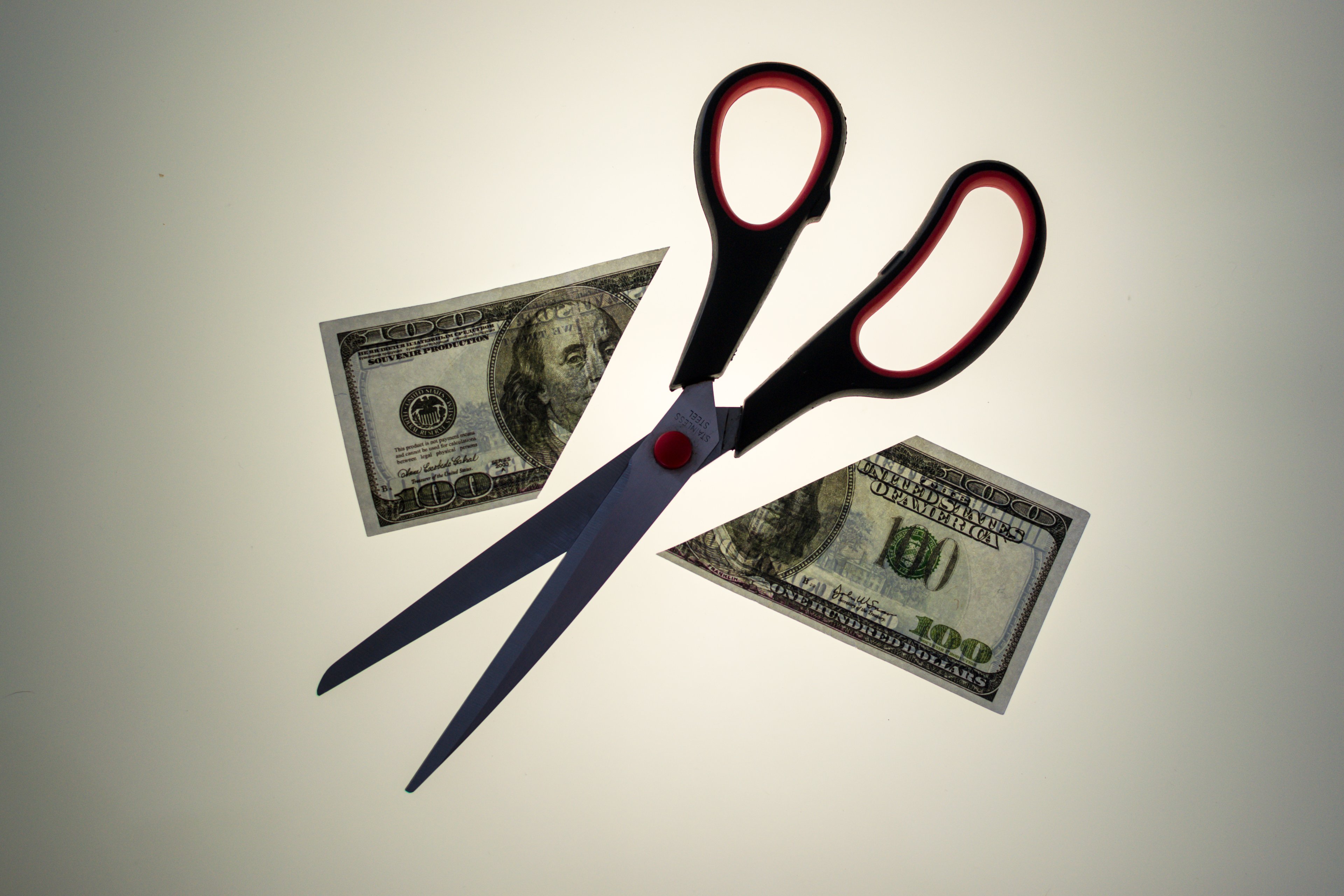 Scissors cutting hundred dollar bill in half