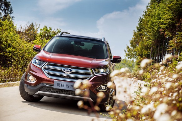 A Ford Edge with Chinese license plates is shown next to a meadow. 