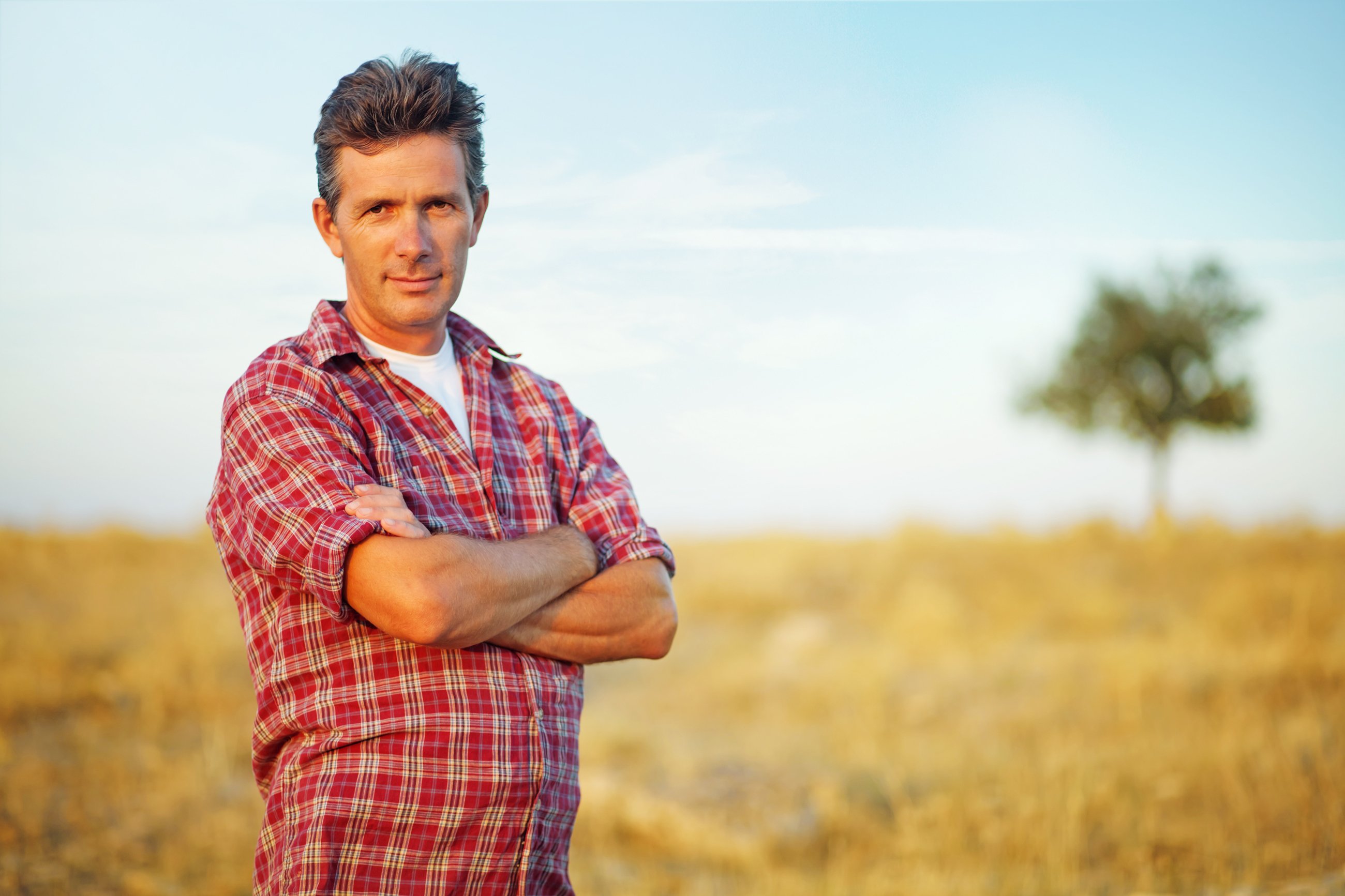 A farmer standing in a field with a rural background.