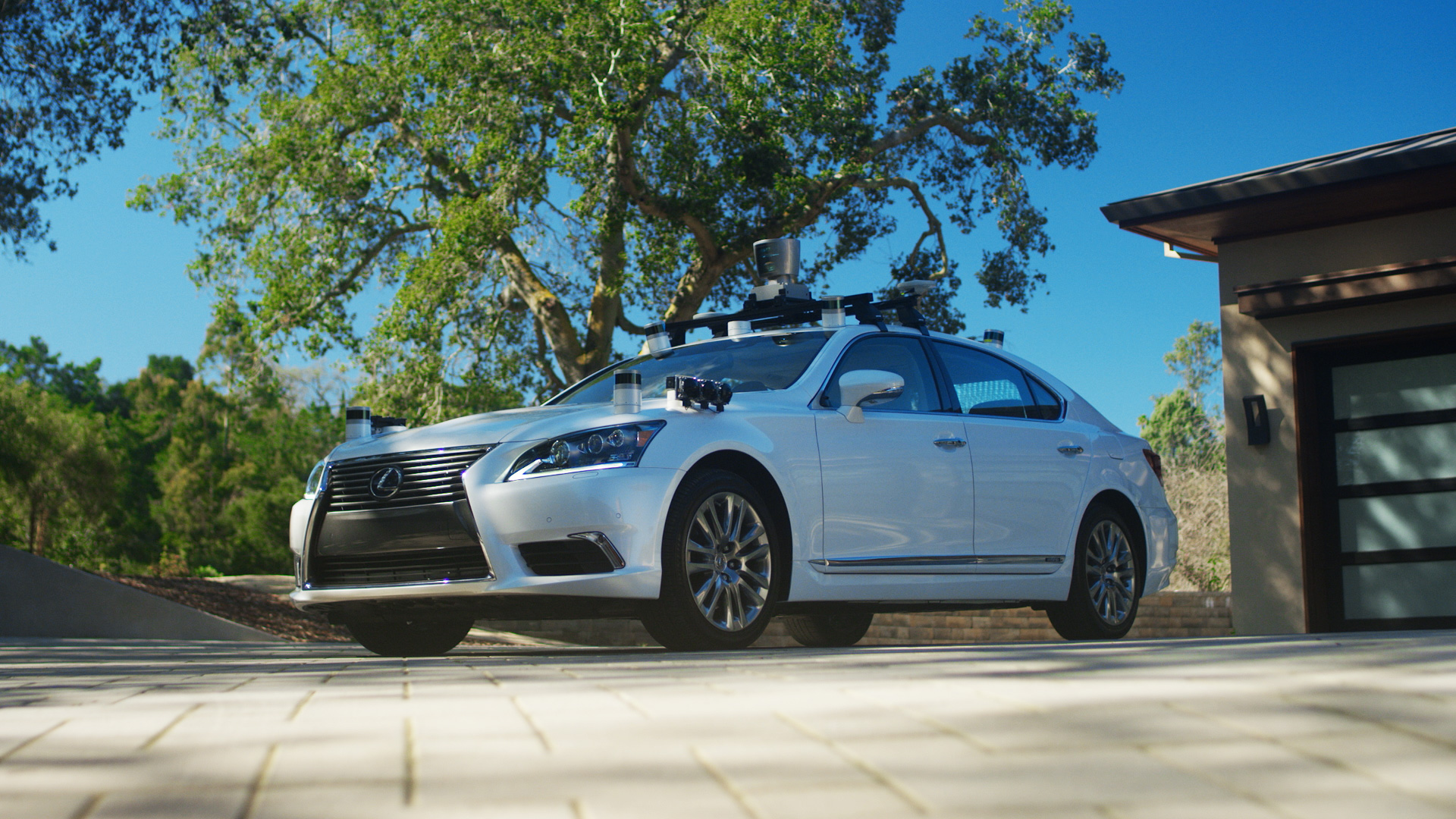 A white Lexus sedan with self-driving sensors in a suburban driveway. 
