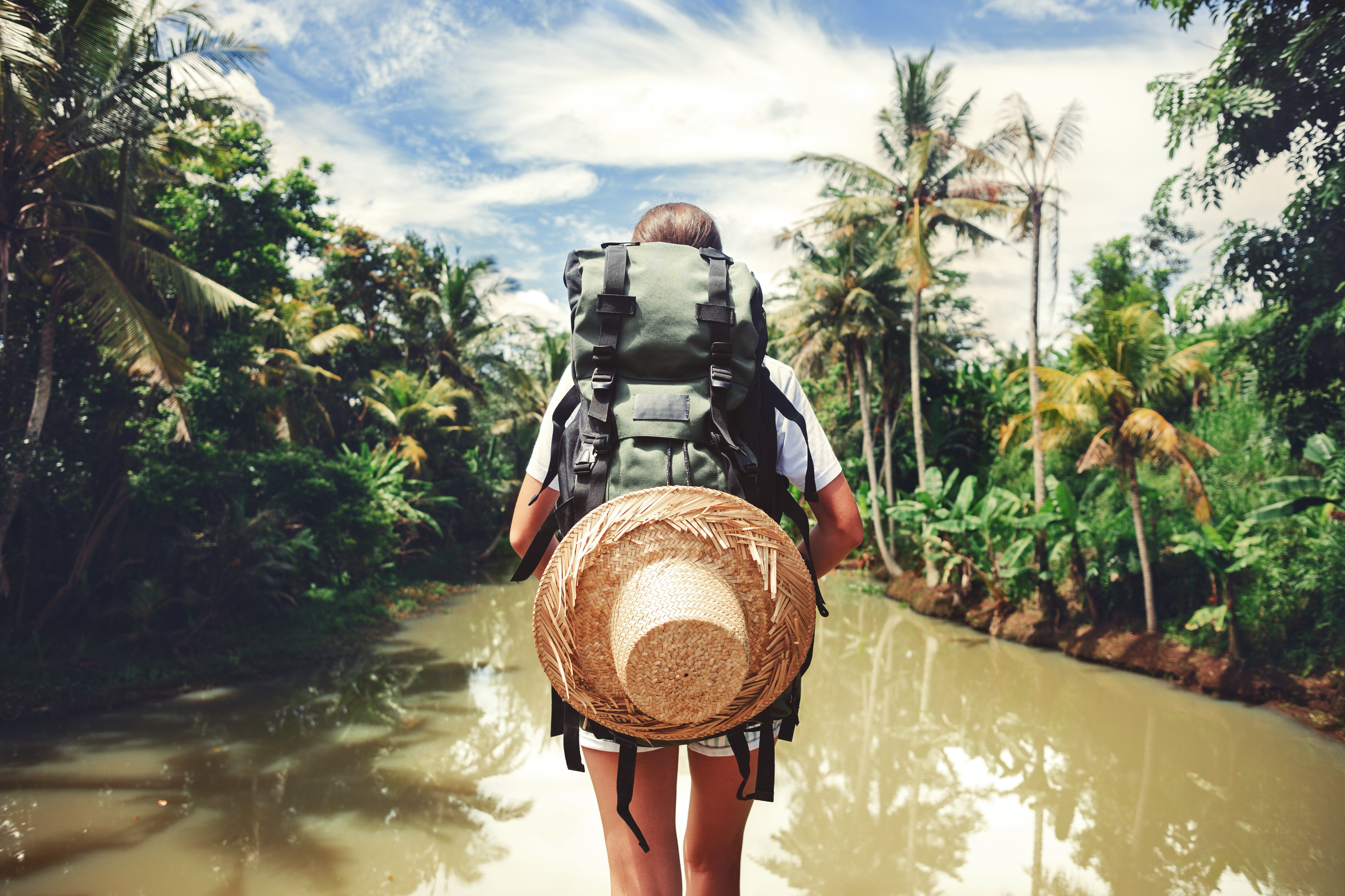 A woman traveler carrying a backpack walking through a muddy river