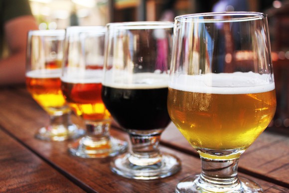 A row of draft beer, poured in glasses, on a bar top.