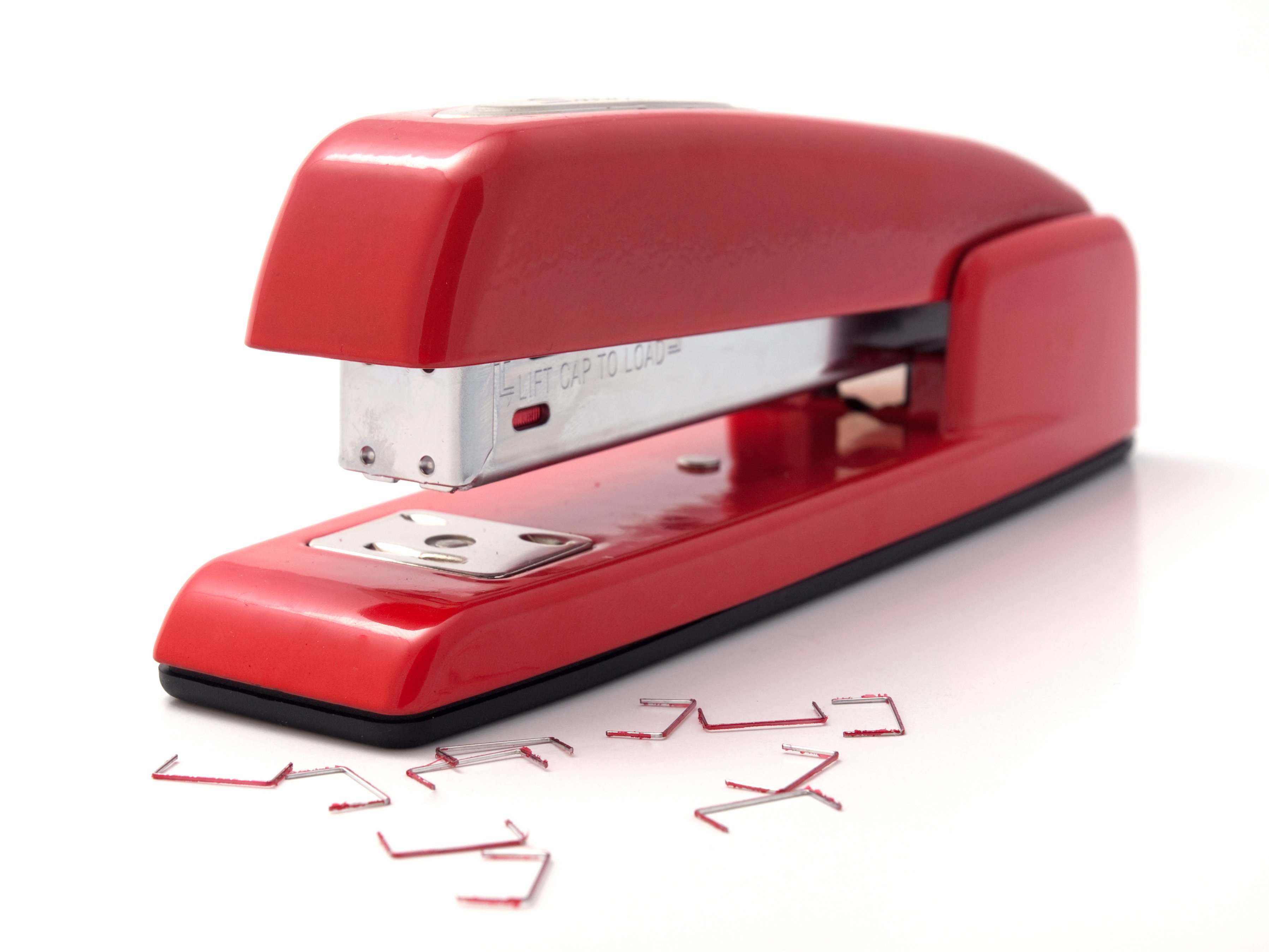 A red stapler with staples strewn alongside it.