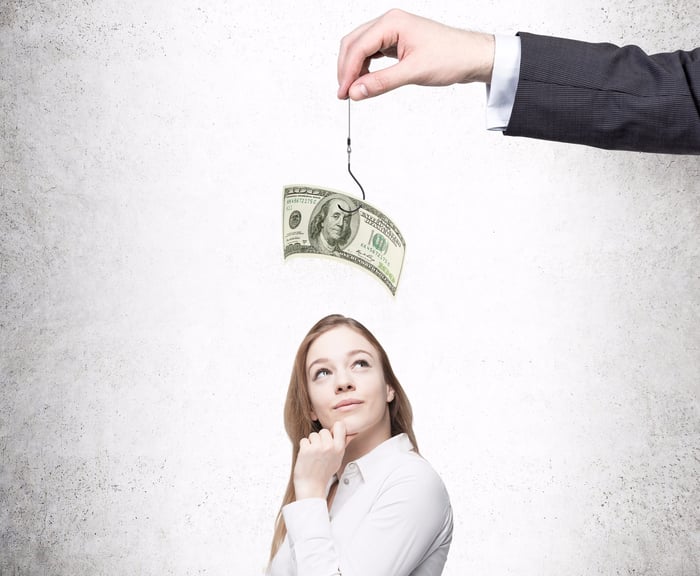 Standing woman seems to be contemplating an arm holding up a fishing hook with a $100 bill on it above her