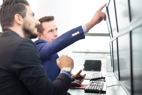 Two traders pointing at computer screens.