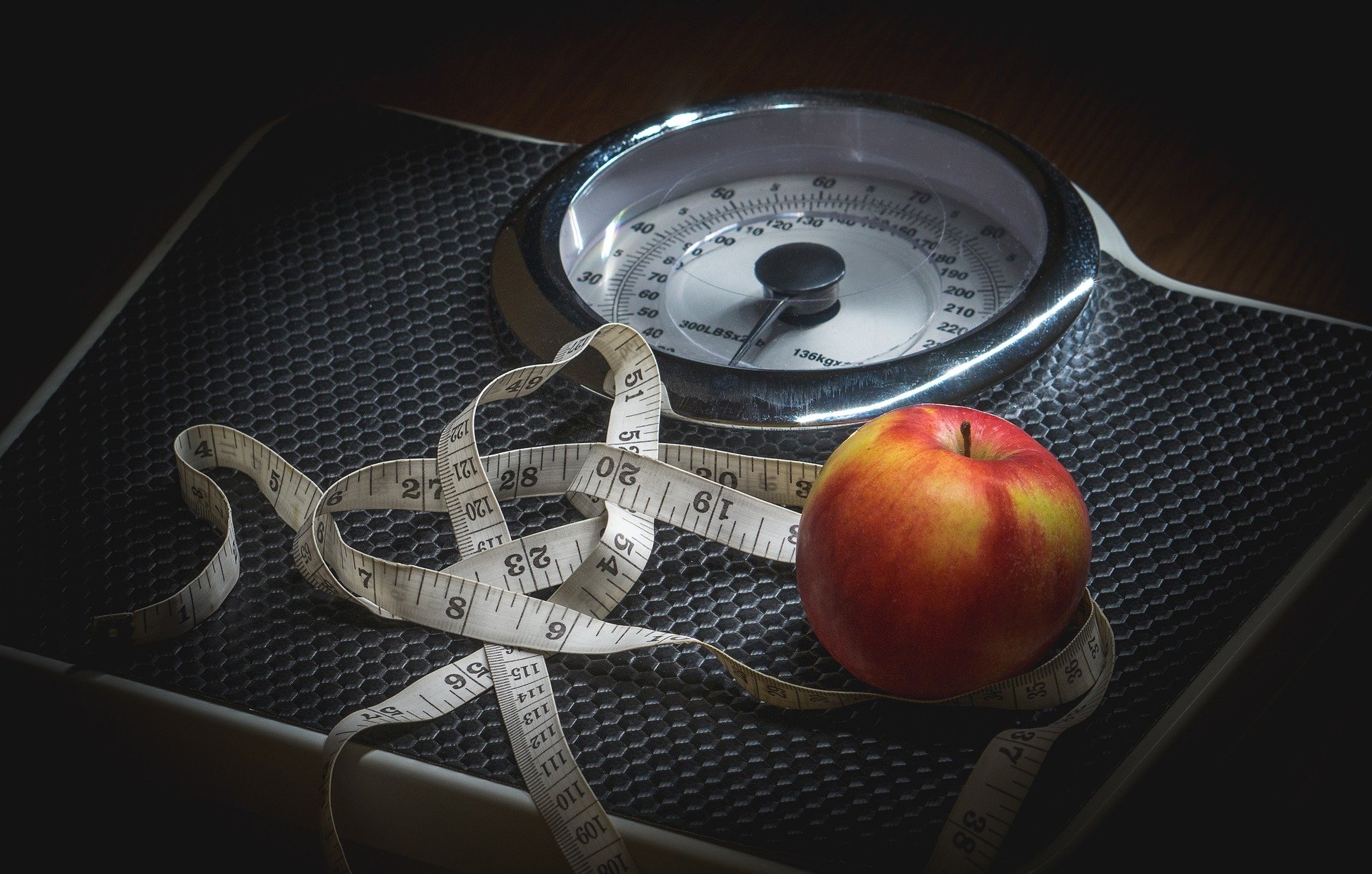 A scale with an apple and a tape measure on top of it.