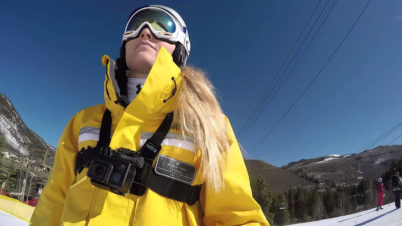 A Vail resorts ski patrol member in a bright yellow jacket looking up a mountain. 