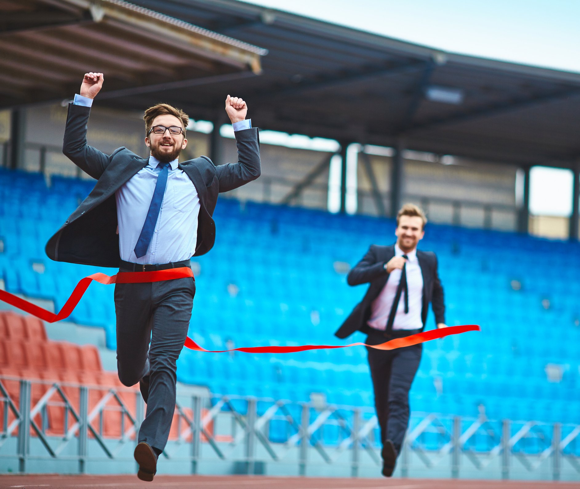Two men in suits racing toward the finish line, with one raising his arms in victory.