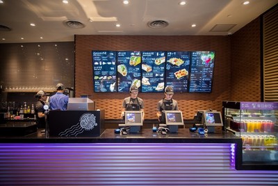 Two employees behind the counter of the new Taco Bell restaurant in Shanghai. The store is a sleek, modern design with ample amounts of the color purple.