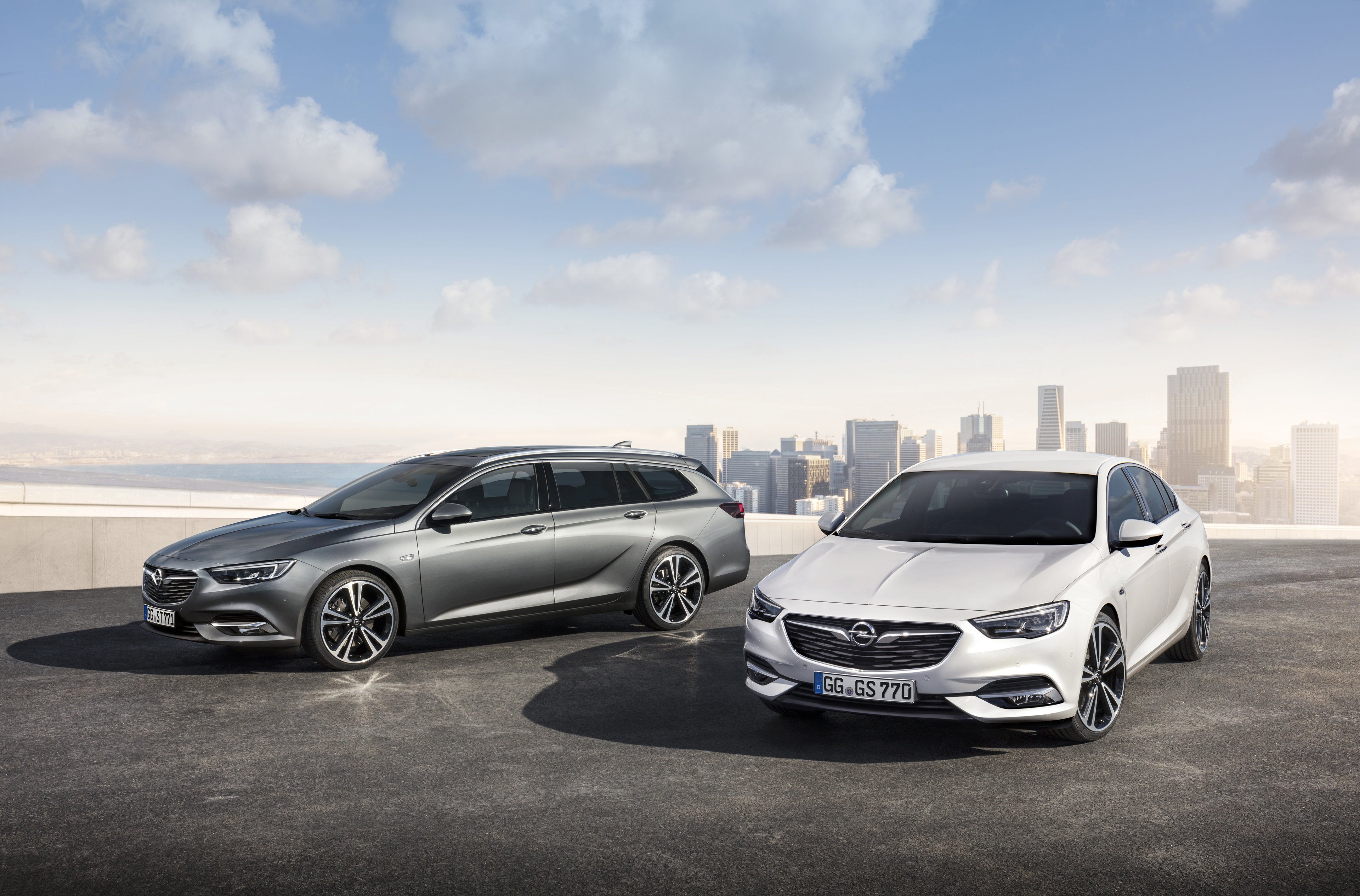 Two 2018 Opel Insignias, a wagon and a 5-door, are shown with a city in the background. 