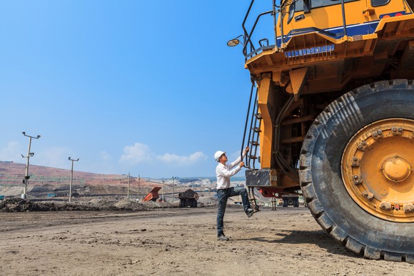 A worker climbs onto a large truck with a tire nearly double his size.