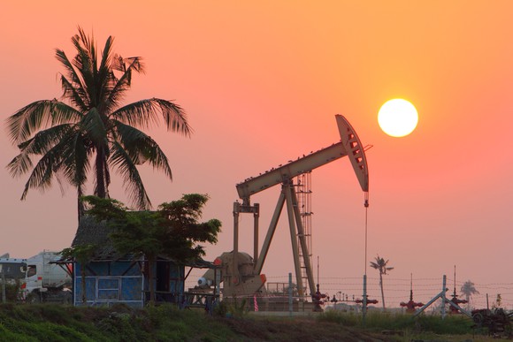 An oil pump near a palm tree at sunset. 