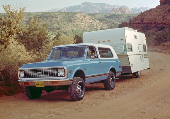 A blue 1969 Chevrolet K5 Blazer pulling a trailer on a dirt road.