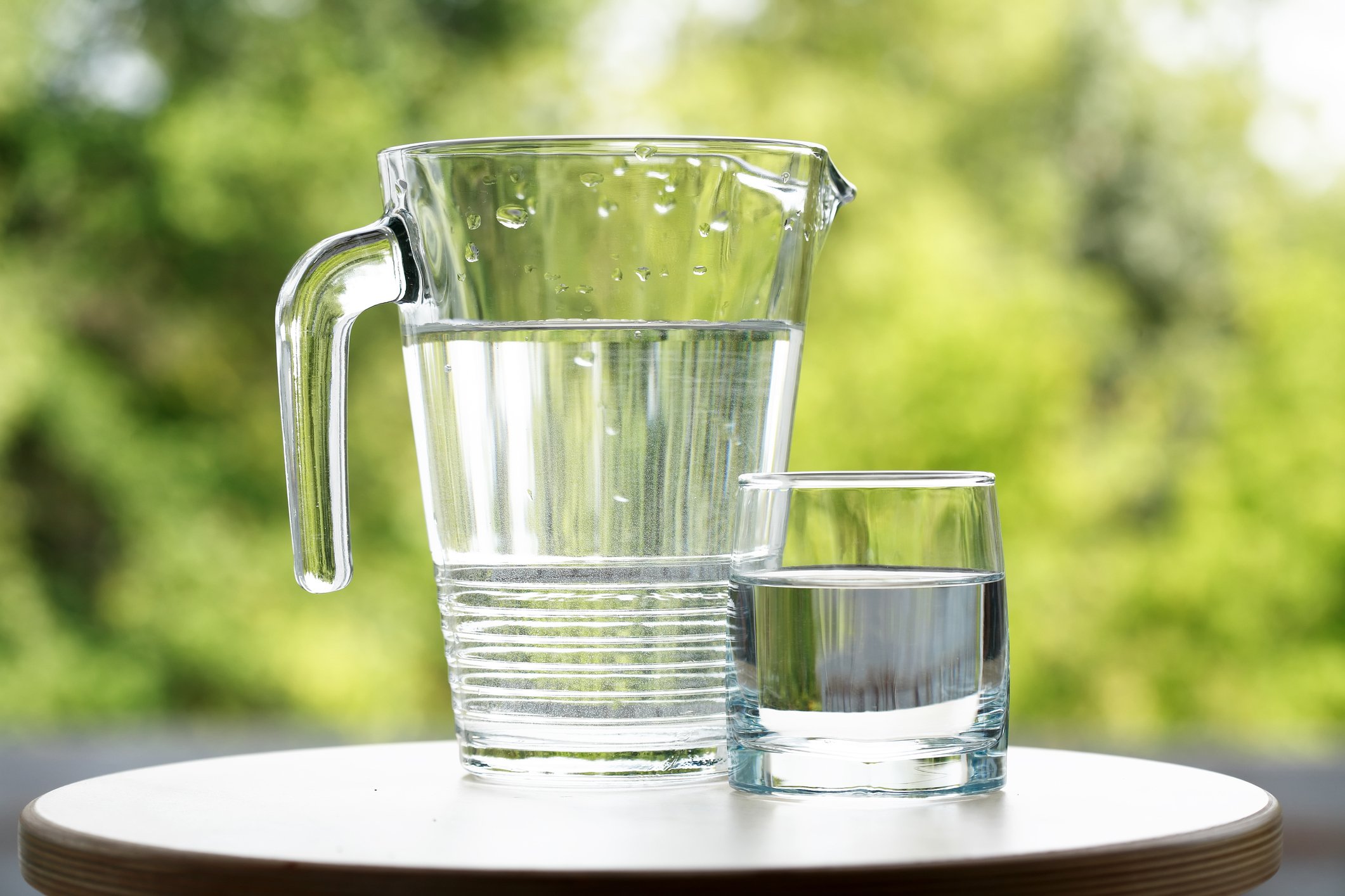 A water pitcher on a table with a glass of water beside it.
