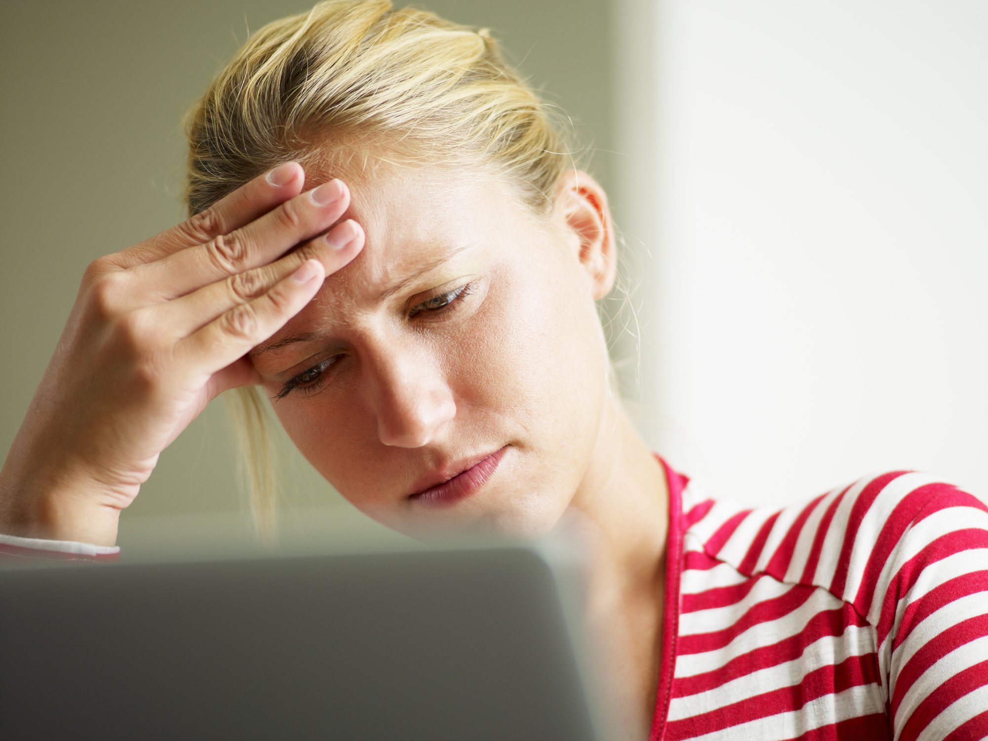 Worried woman looking at a laptop with her hand resting on her forehead