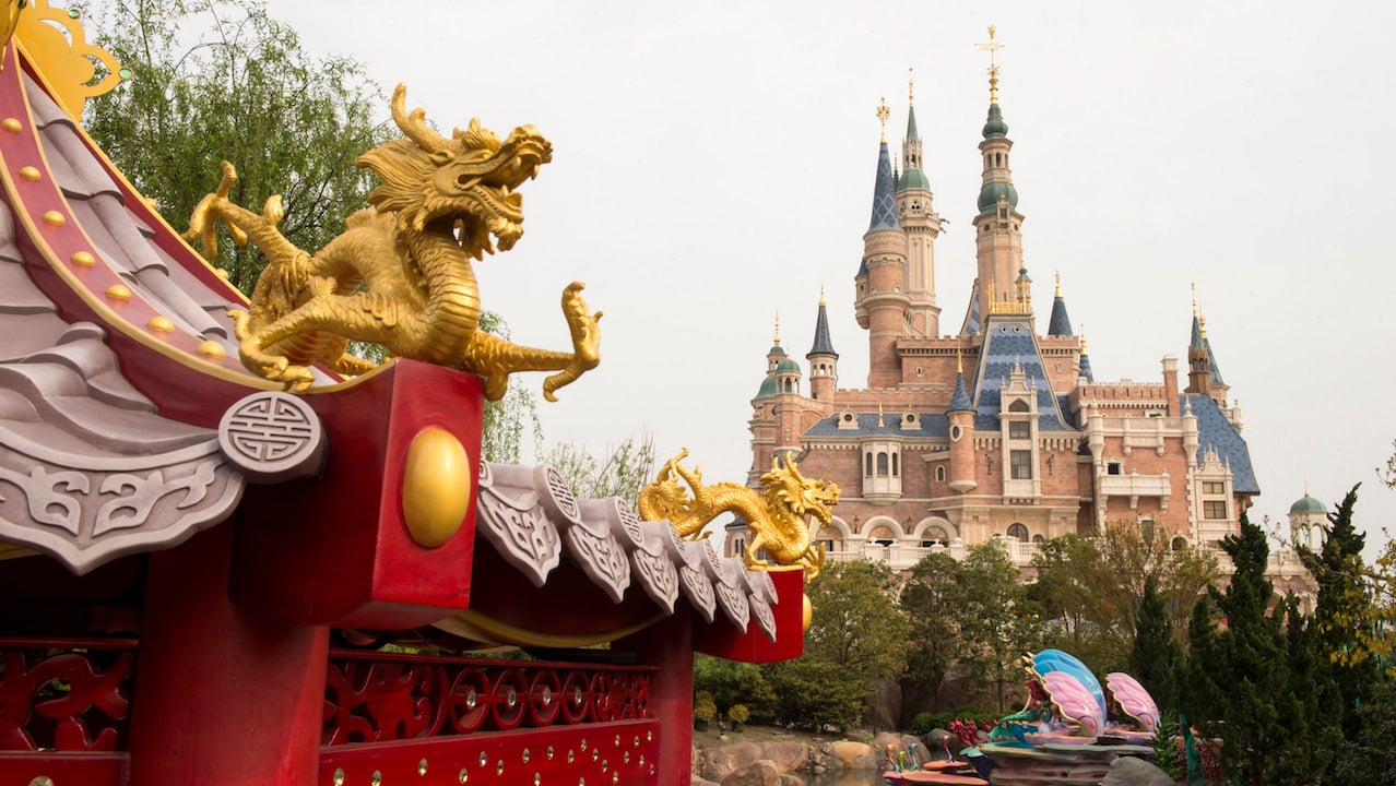 A dragon carving smiles in the foreground in front a castle at Disney Shanghai