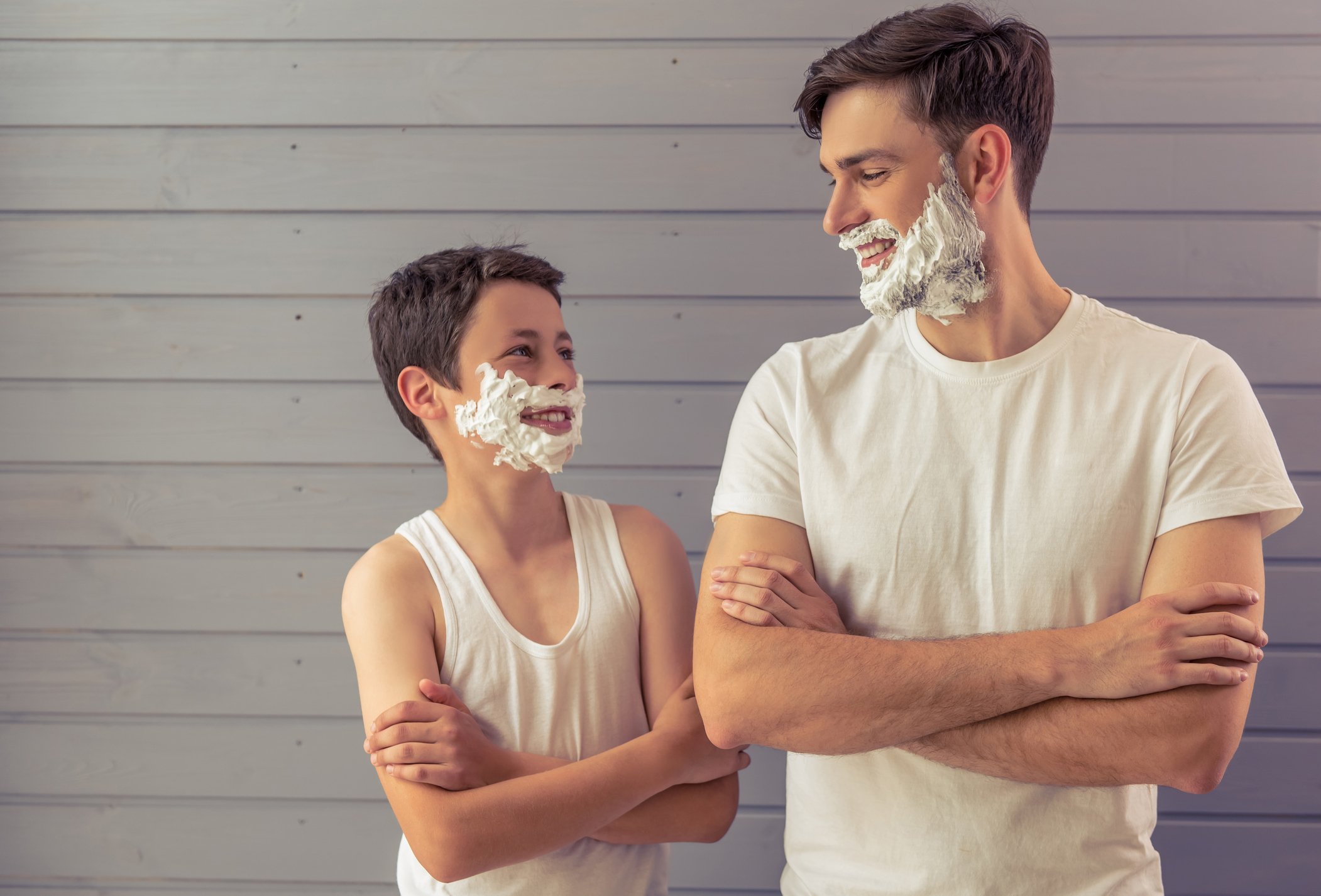 A father and son looking at each other with shaving cream on their faces.