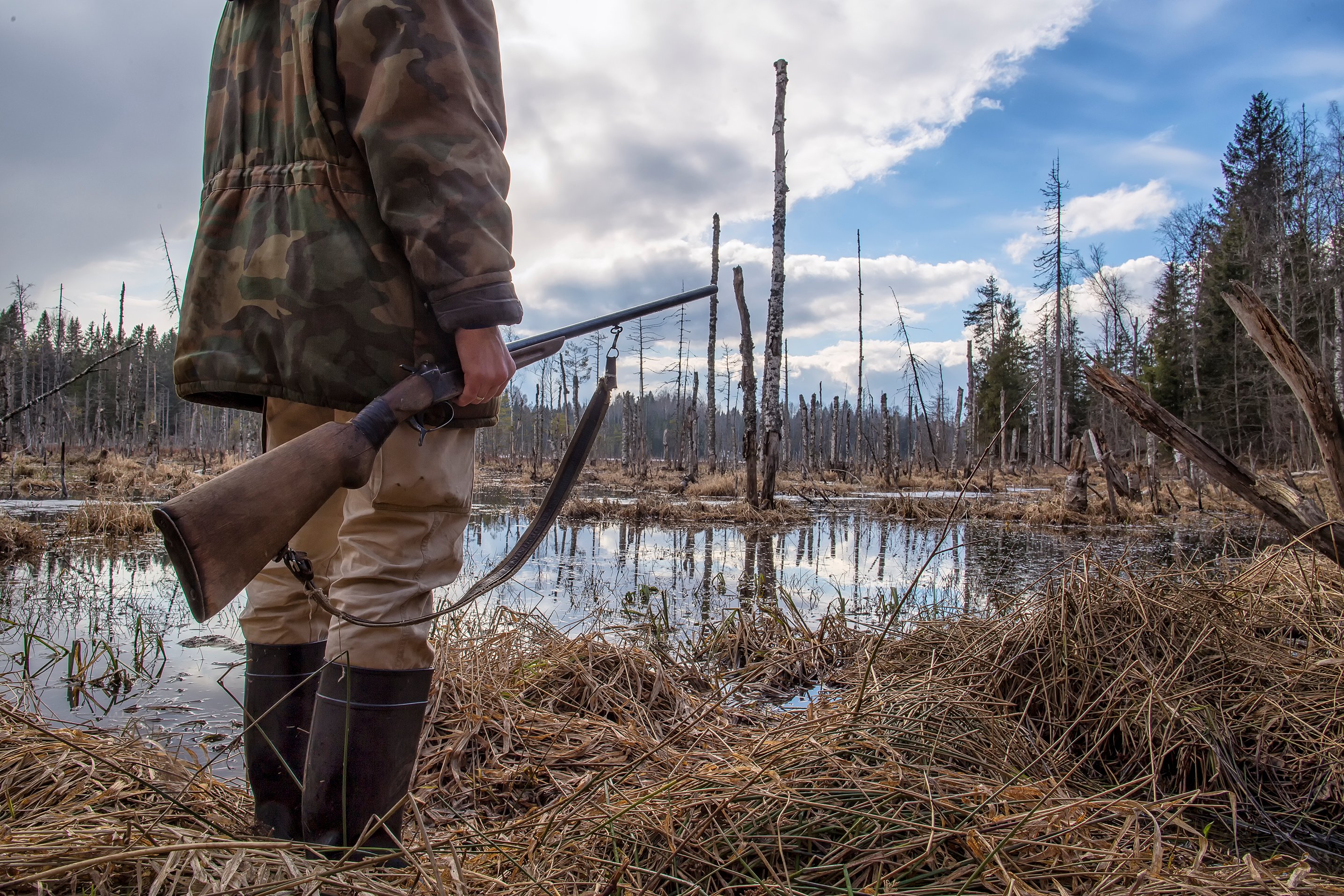 Hunter standing in water, holding a shotgun in his right hand