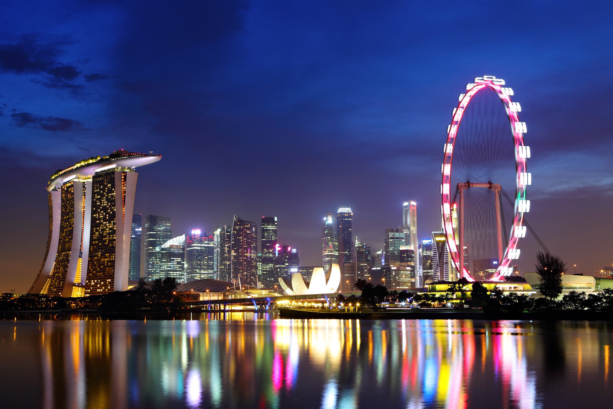 The Singapore skyline with reflections of the buildings and ferris wheel in the night water.