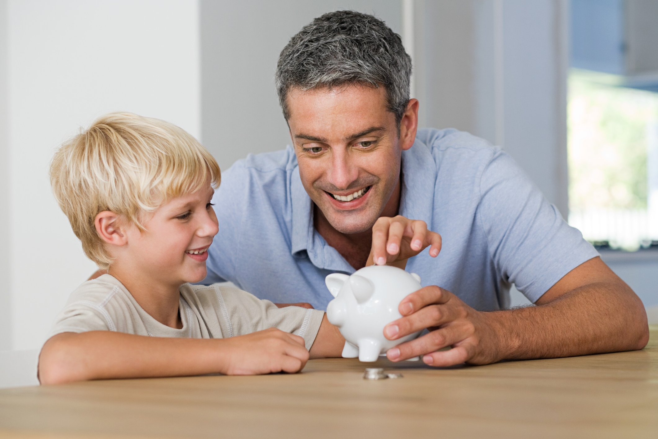 Father and son placing coins in a piggy bank.