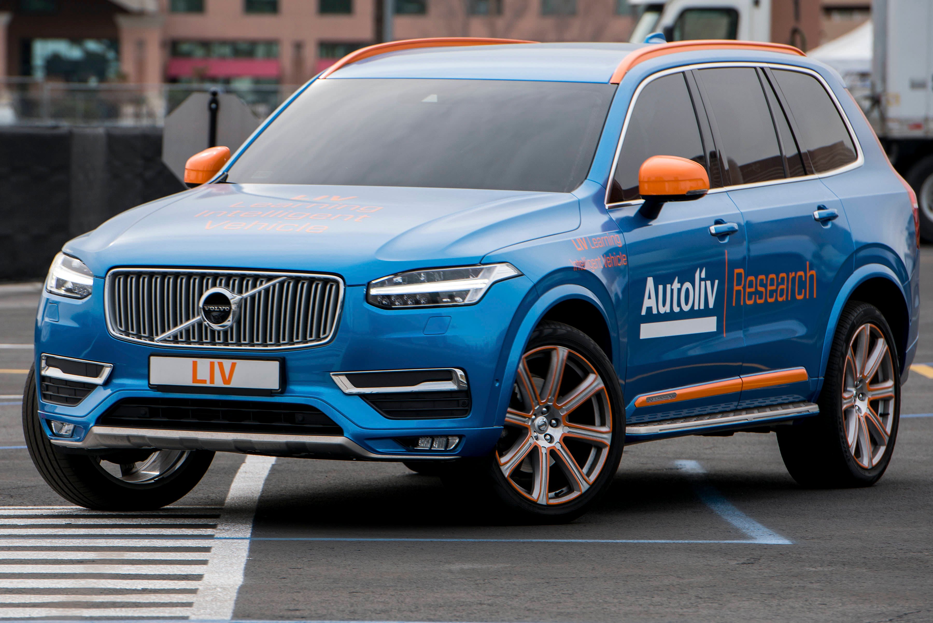 A blue Volvo SUV with Autoliv emblems on a city road.