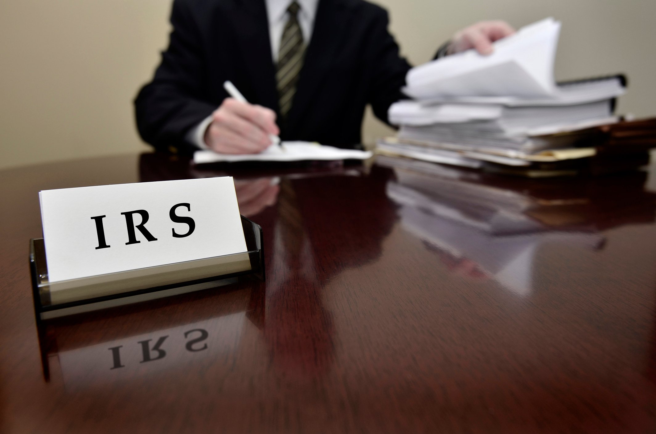 torso of man in suit behind shiny desk with business card holder that says IRS