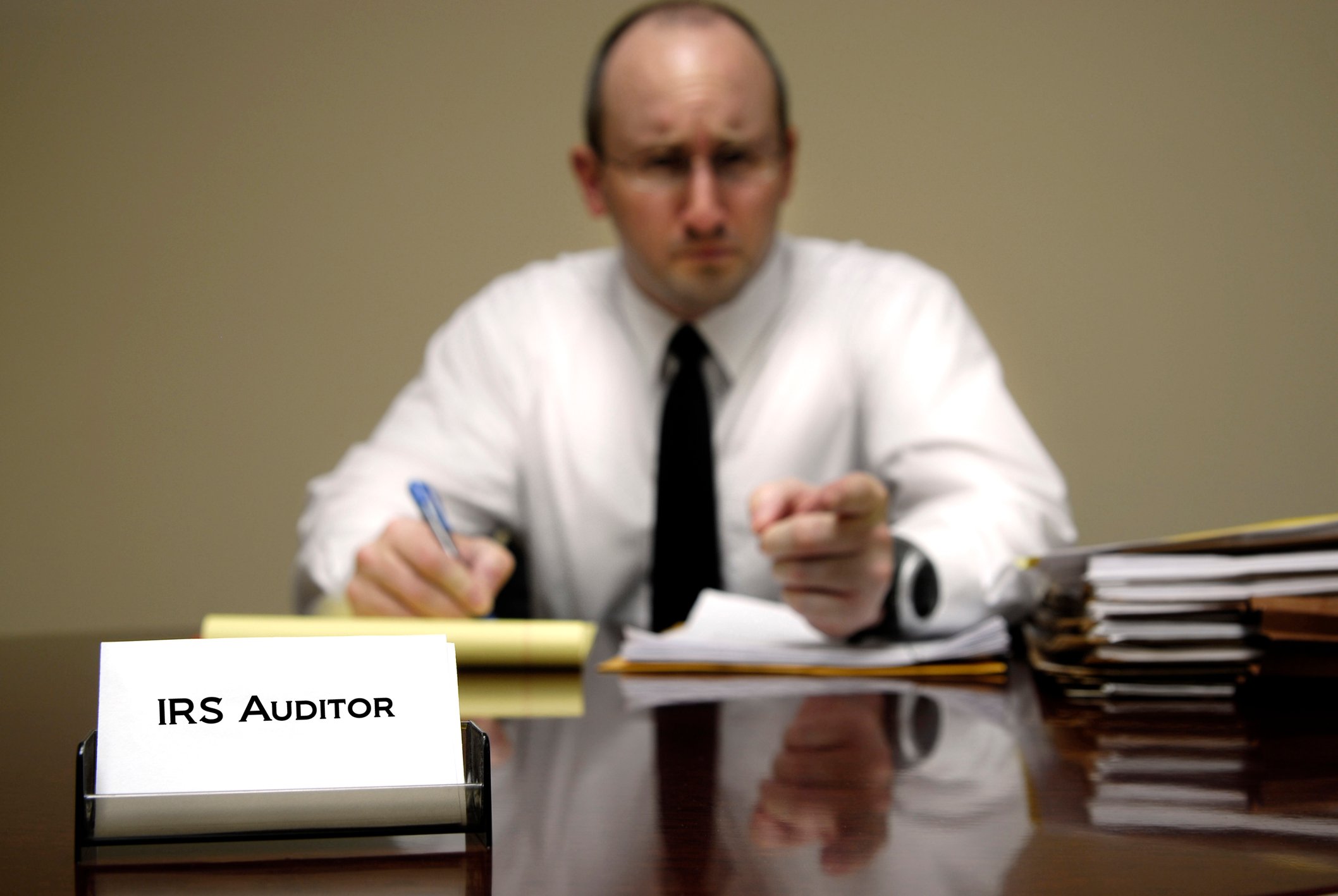 Man at desk labeled "IRS Auditor" looking a little menacing
