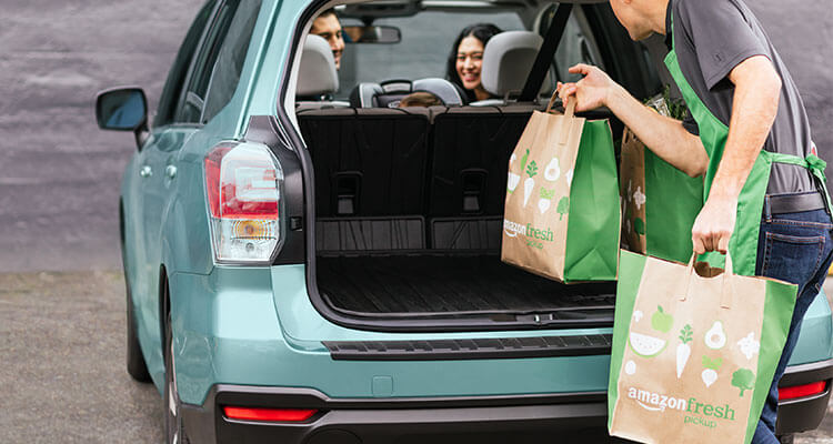 An AmazonFresh worker loads bags into a trunk.
