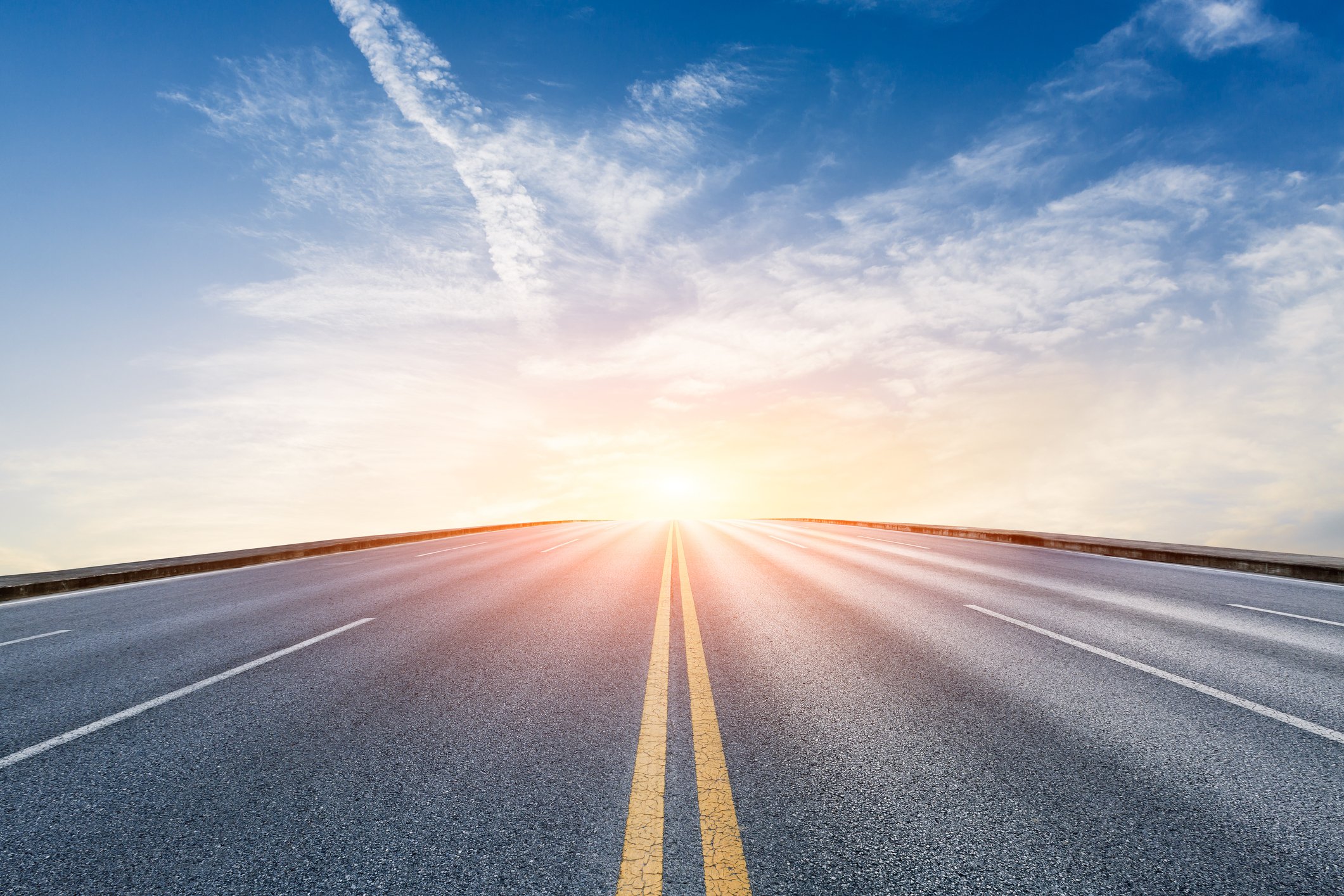 A road with the sun rising in the distance.