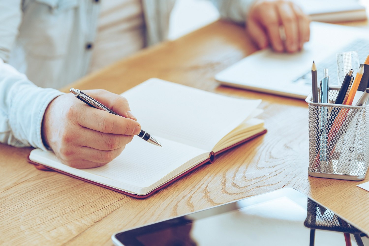 Man sitting at a desk with pen in hand, poised over a blank notebook.