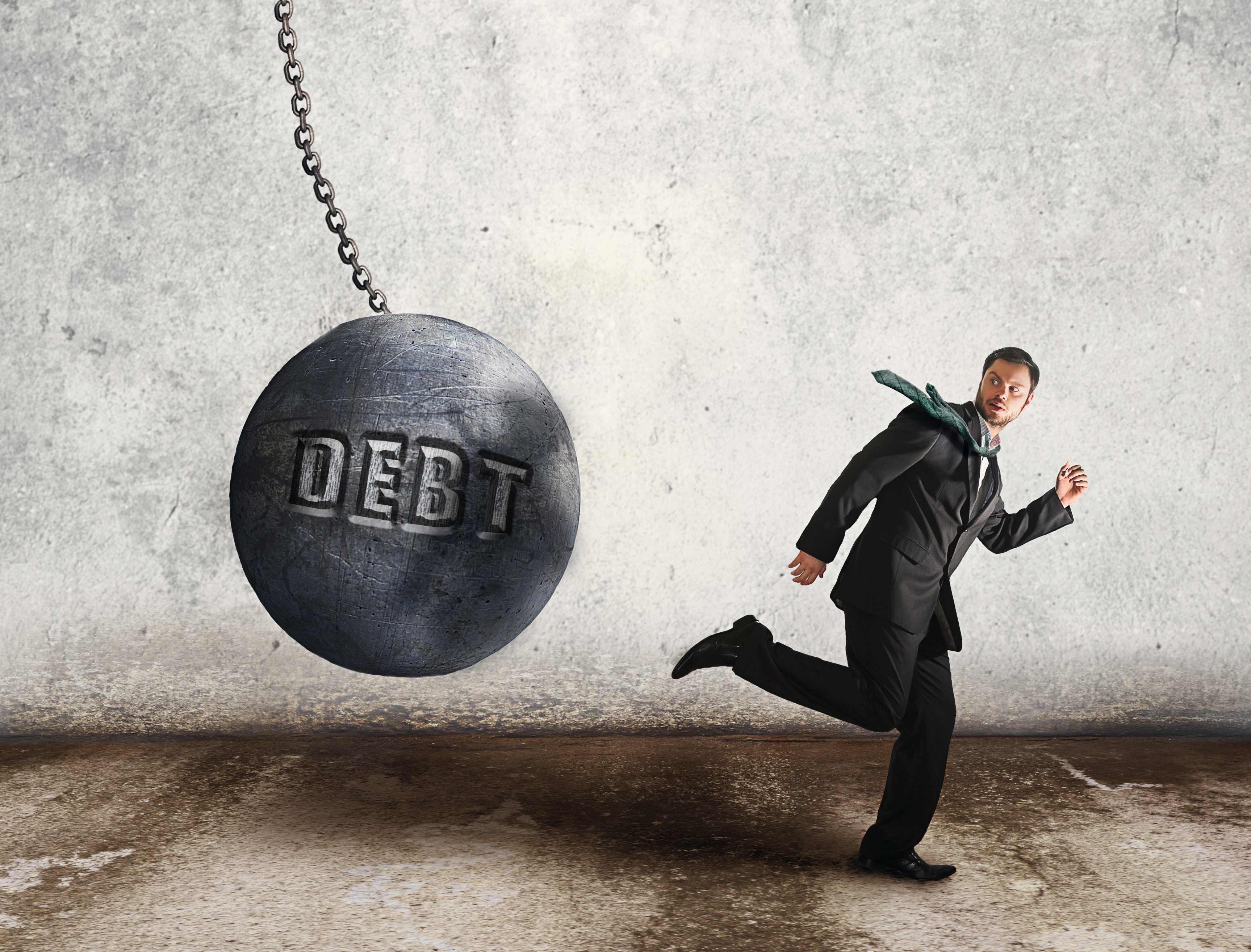 Wrecking ball with "Debt" written on it, headed for businessman.