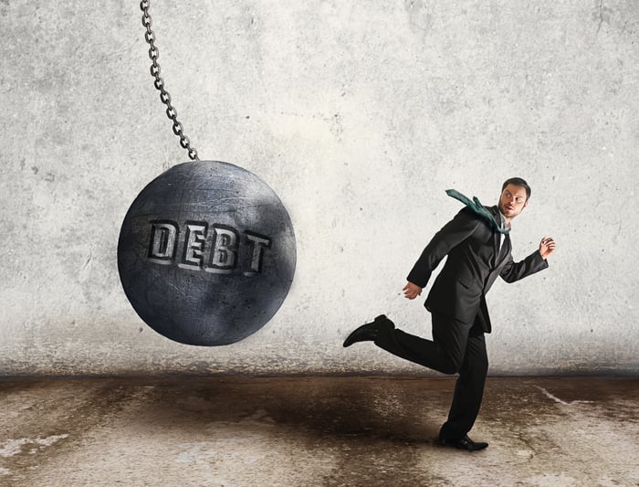 Wrecking ball with "Debt" written on it, headed for businessman.