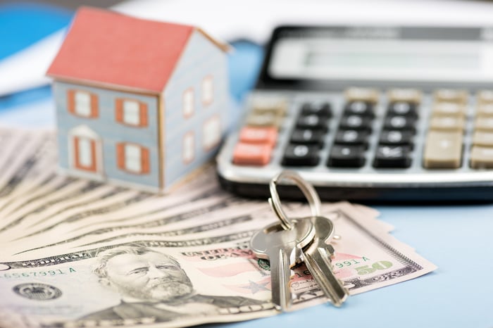 Miniature house, keys, and calculator with stack of money.