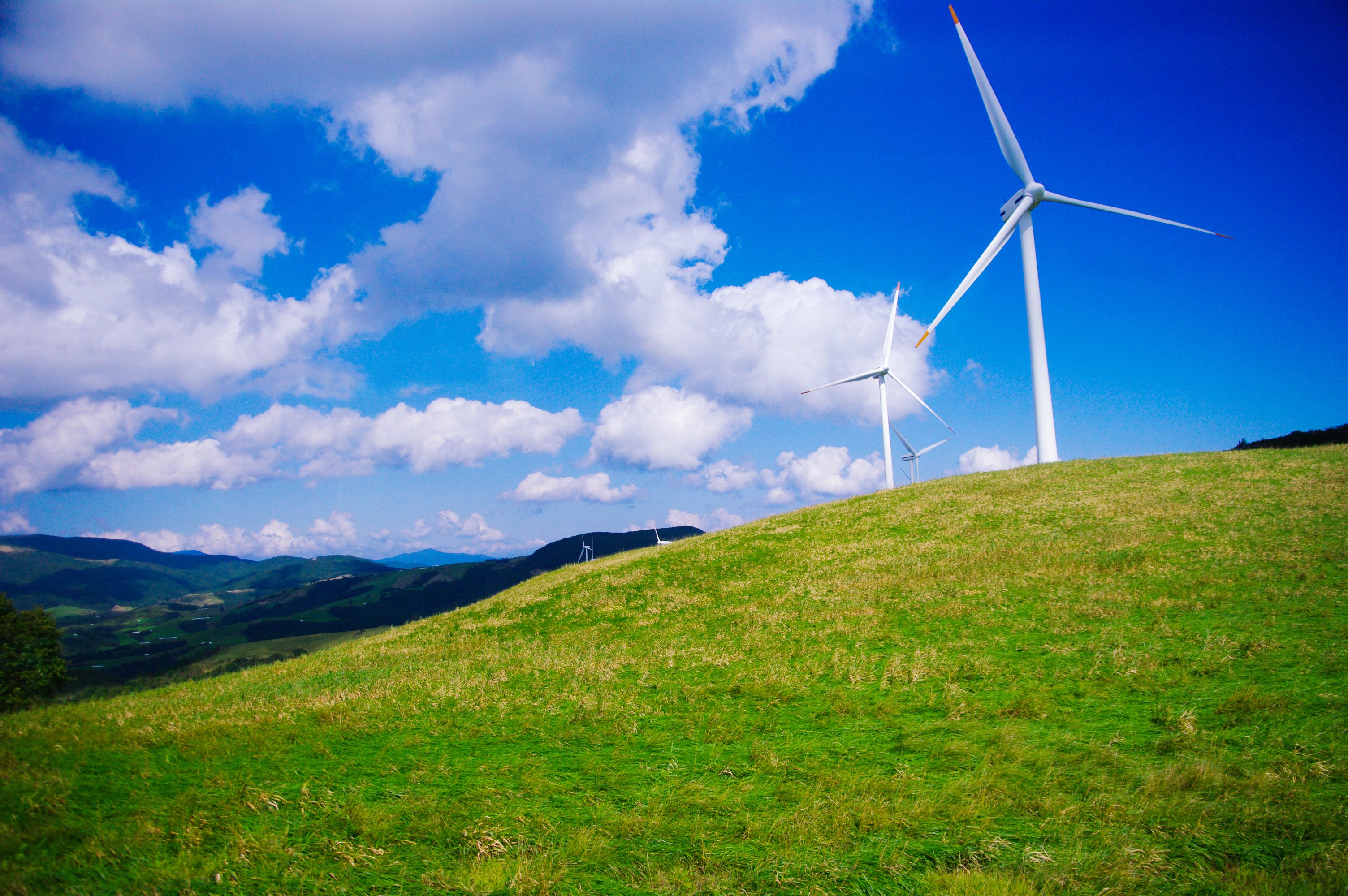 A series of wind turbines on rolling, grassy hills.