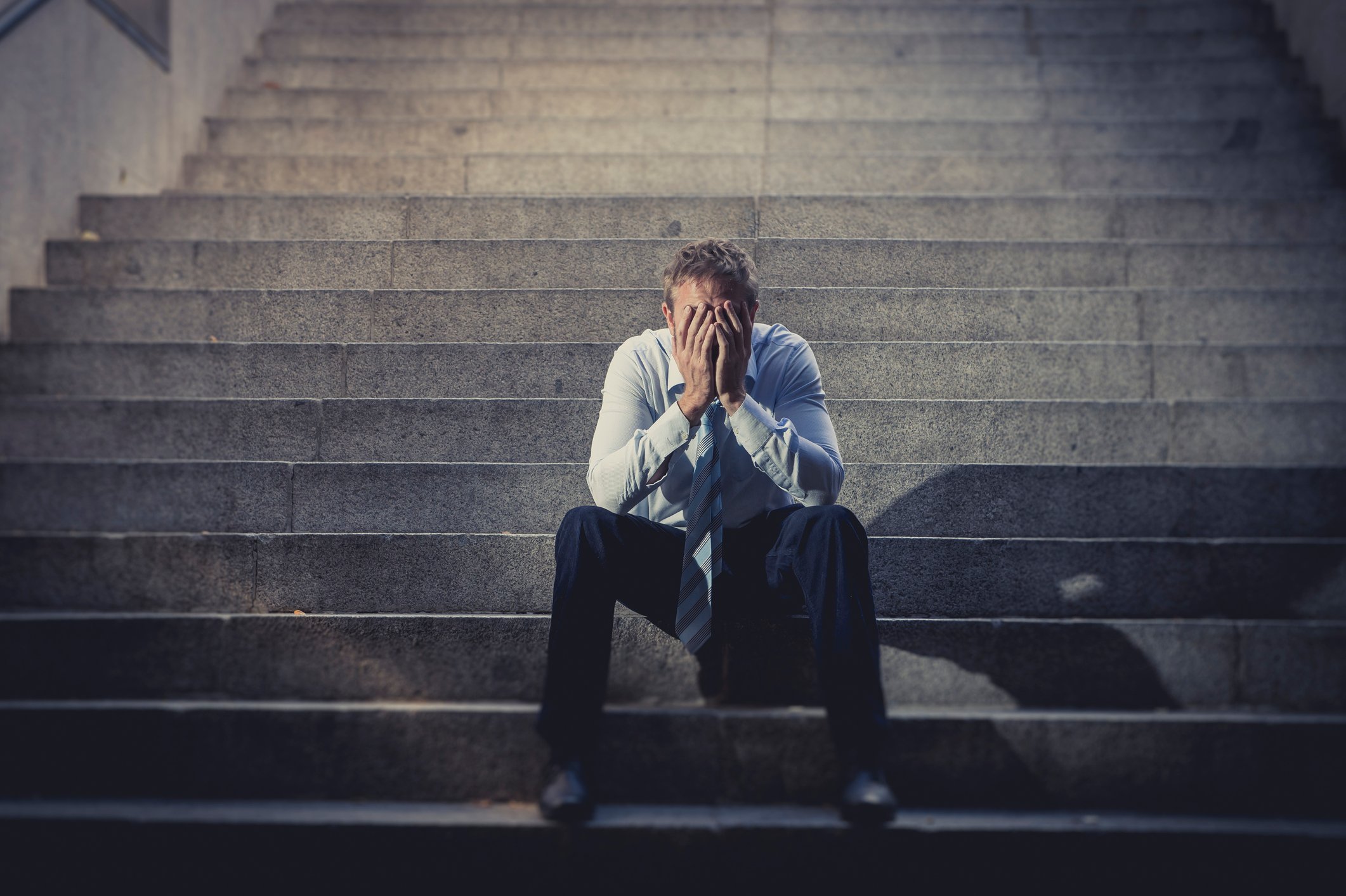 A man with his face in his hands, sitting on the steps outside of a courthouse.