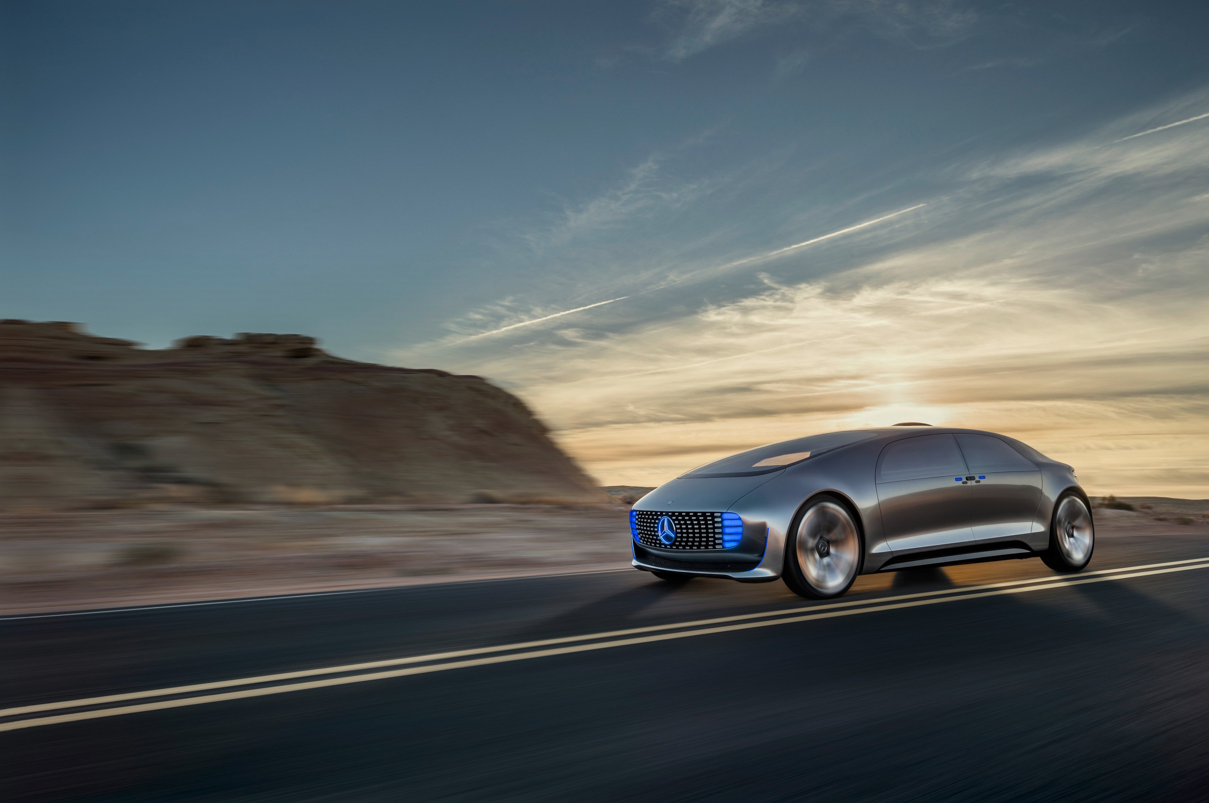 The Mercedes concept vehicle, a futuristic-looking silver sedan, is shown on a country road.