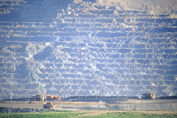 Mining vehicles are dwarfed by the large walls of the mine.