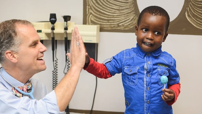 A doctor hi-fives a patient that is holding a lollipop.