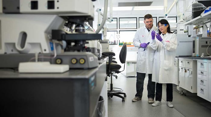 A man and woman in lab coats examine a vial of liquid. 