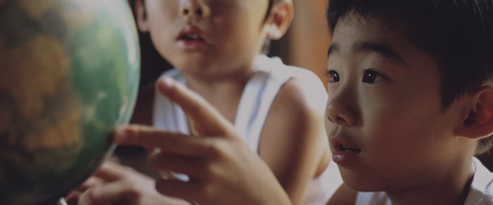 Two young boys look in wonderment at a globe.