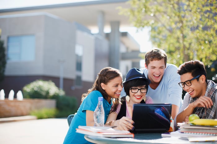 Group of college students gathered around a laptop.