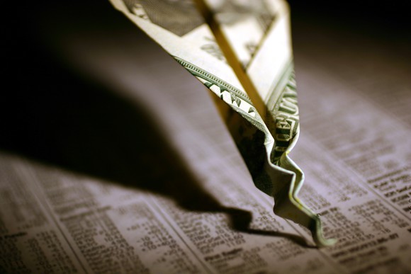 Paper airplane made of money crashing into newspaper stock page