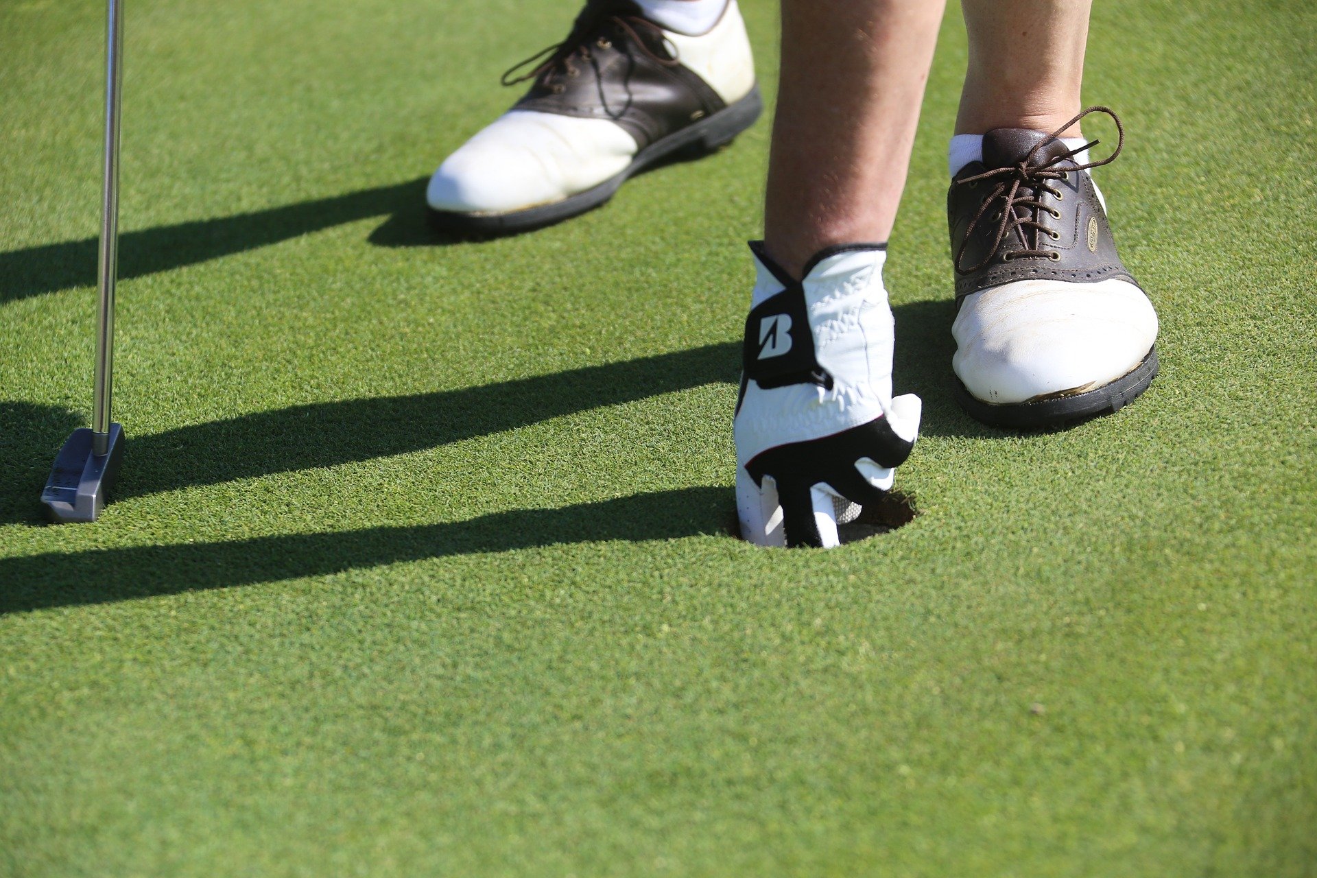 Two feet in golf shoes on putting green, placing ball