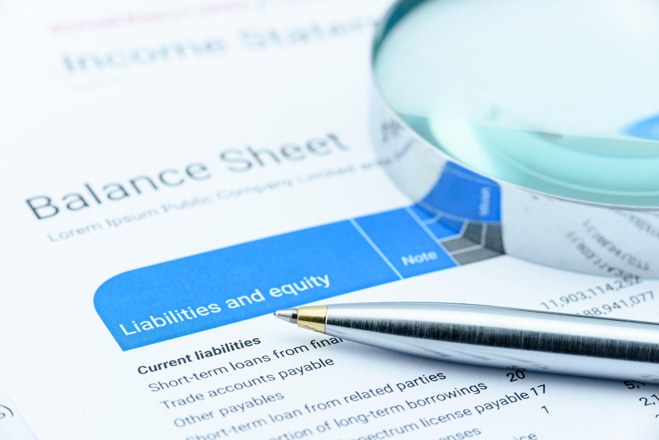 Paper with "balance sheet" written on it, with a pen and magnifying glass placed on it