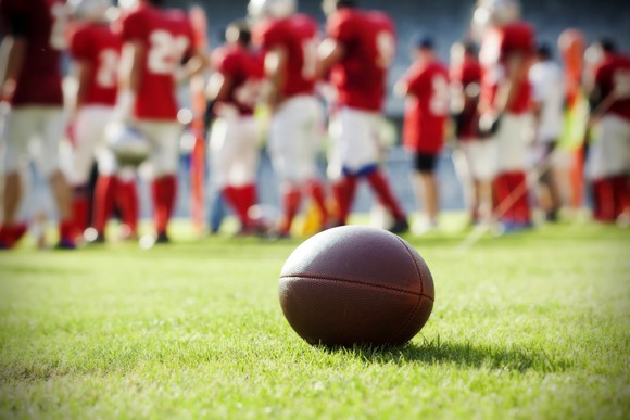 Close-up of a football with team huddled in the background.