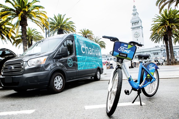 A Chariot shuttle bus and Ford-branded bicycle at rest in an urban setting.