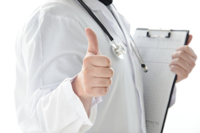 A doctor with a clipboard giving the thumbs-up sign. 