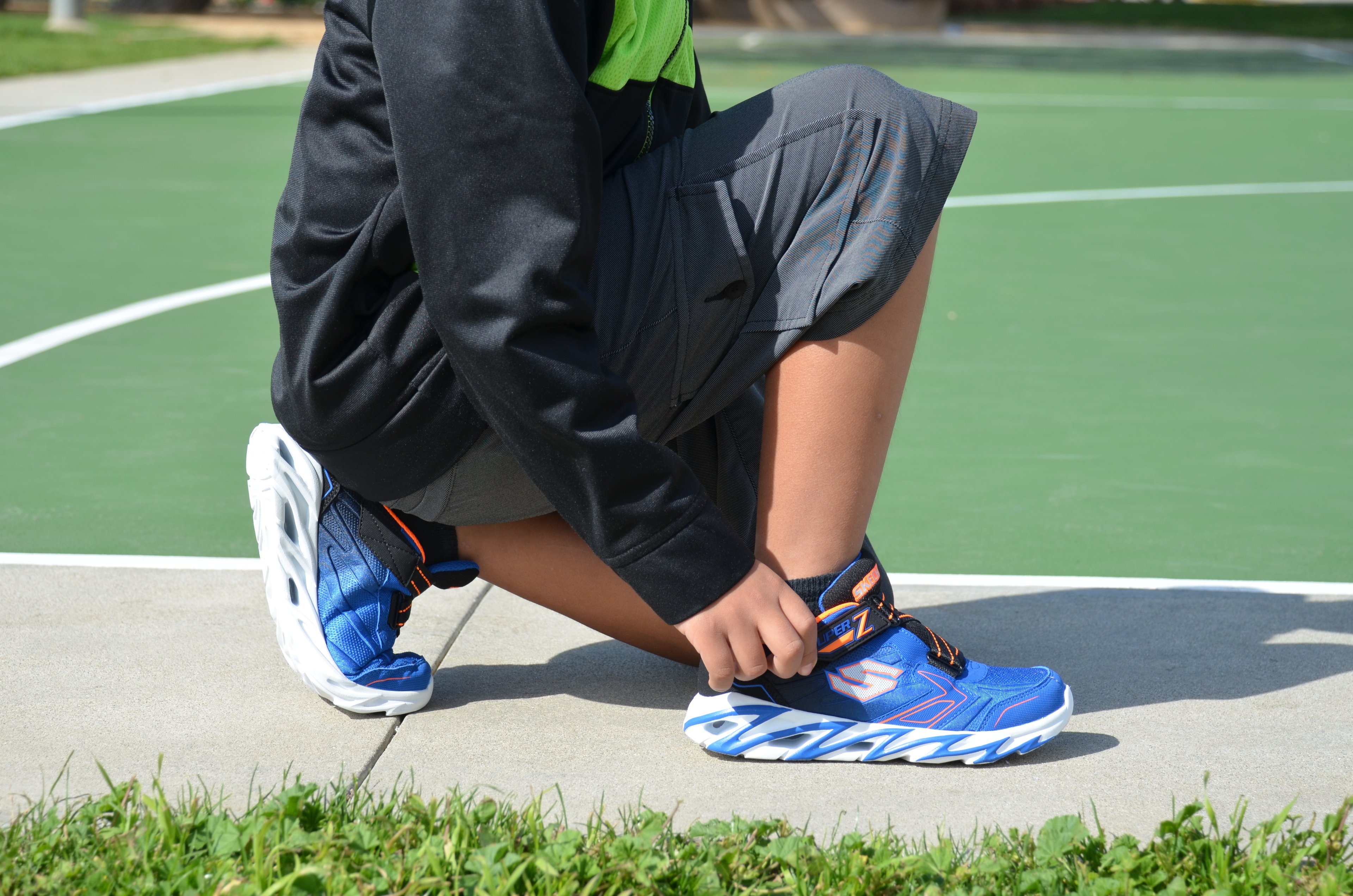 A person adjusting Skechers shoes at a basketball court.